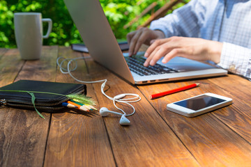 Man arms typing on keyboard at natural hardwood desk with green flora background many electronic...
