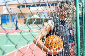 young man with the basketball behind a fence
