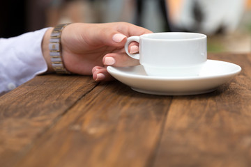 Female hand holding white coffee mug at grunge wood desk