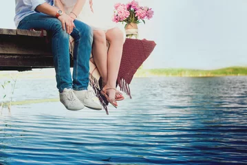Fotobehang Pretty strong young loving couple sitting on the bridge over the river, next to a bouquet of peonies, lifestyle, concept, love, tenderness © tatyana_k