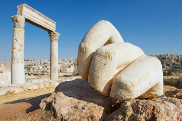 Stone Hercules hand at the antique Citadel in Amman, Jordan. At the background: ruins of the Hercules temple and Amman city.