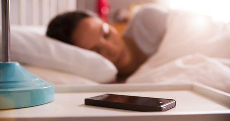 Woman Asleep In Bed Using Alarm On Mobile Phone