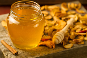 glass jar of Linden honey with drizzler, cinnamon, apples on wooden background