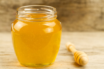 glass jar of honey with drizzler on wooden background