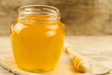 glass jar of honey on jute fabric with drizzler on wooden background