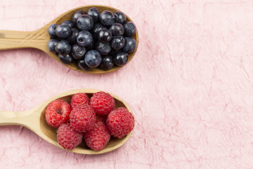 Blueberries and raspberries in a wooden spoon on a pink napkin. Healthy vegetarian food, diet.