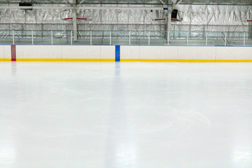 View across the empty ice of an indoor hockey rink with metal bleachers