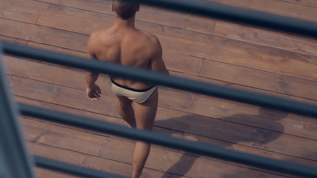 Sexy man in swimming trunks going on the wooden pier outdoors to