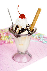 Chocolate Sundae on Pink Background - Vanilla ice cream, topped with hot fudge chocolate, whipped cream, a maraschino cherry, and a round cookie.