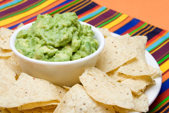 Fresh Guacamole and Chips – A bowl of fresh guacamole, surrounded by corn tortilla chips. Colorful background.