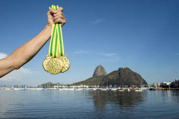 Hand of first place athlete with Brazil colors wristband holding gold medals at Botafogo Beach Rio...