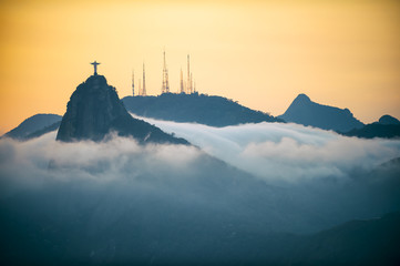 Corcovado mountain Christ the Redeemer standing in golden sunset above swirling mist clouds Rio de...