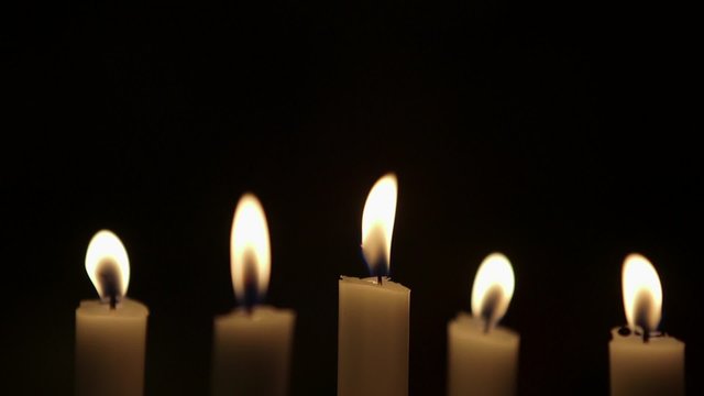 Rack focus on lit candles against black background. Flames are being blown due to wind in studio.
