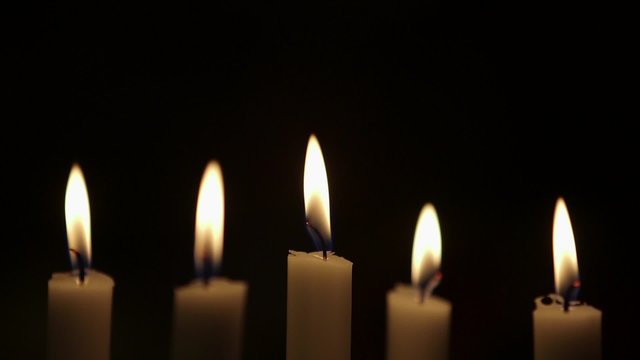 Rack focus on lit candles against black background. Flames are being blown due to wind in studio.
