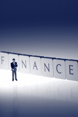 Fototapeta premium Miniature businessman finance. Miniature scale model businessman standing in front of the word finance on tiles.