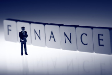 Fototapeta premium Miniature scale model businessman standing in front of the word finance on tiles.