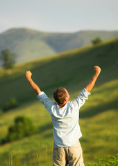 A man stands with his arms outstretched in an open field - success.