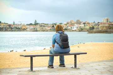 Girl with a backpack sitting on the coast and looking to the opp