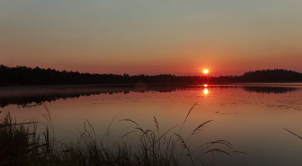 Raising sun under early morning coniferous wood lake 