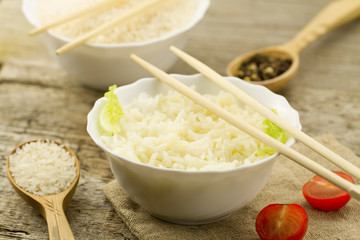 White plate of cooked long-grain rice on wooden background. Healthy eating, diet, vegetarianism.