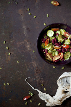 summer salad with fresh vegetables and seeds on bowl on a rusty surface with cloth 