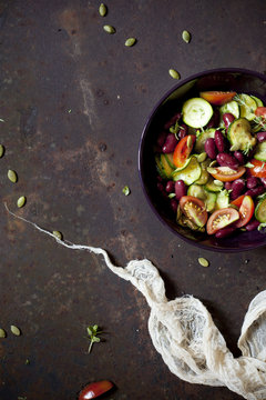 summer salad with fresh vegetables and seeds on bowl on a rusty surface with cloth 