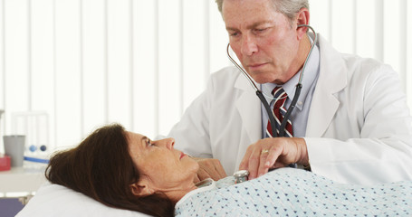 Senior doctor listening to mature patient's heart