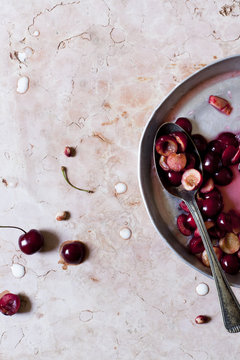 juicy cherries cut in half on a round tray with spoon on marble surface