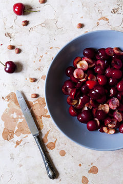 cutting in half juicy cherries on plate on marble surface with a knife