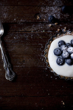 close-up of one blueberries and yogurt cream tart on wooden surface with spoon
