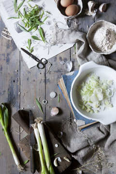 sliced and whole fresh spring onions on rustic table with ingredients