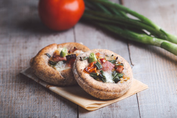 Mini pizza with bacon, onion and tomato.