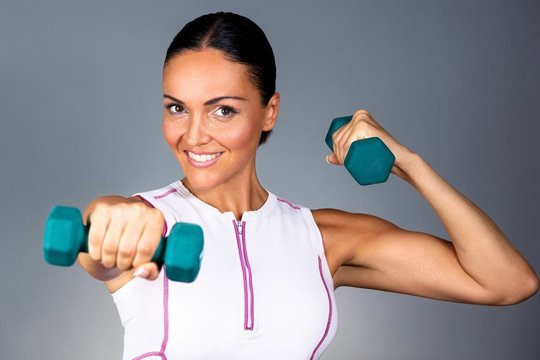 Young fitness woman training with weights against grey background.