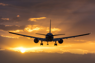 Fototapeta na wymiar Plane flying towards the runway during a cloudy sunrise.