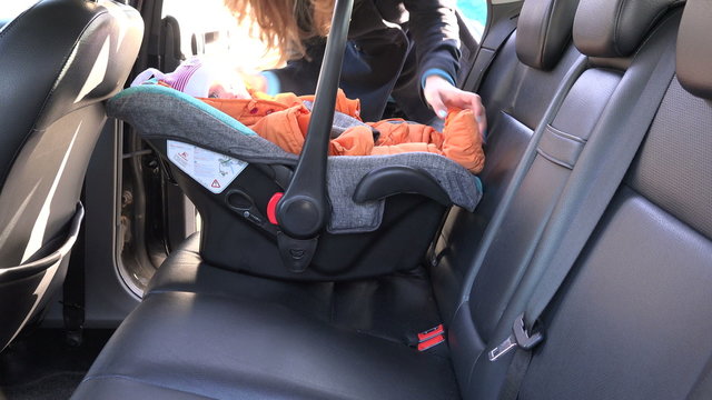 Loving mother woman put baby safety chair with infant child on back car seat and fasten with safety belt. Safe baby transportation inside automobile. 4K UHD video clip.
