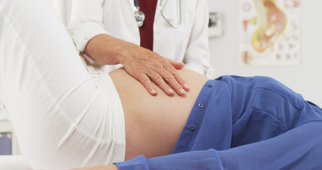 Senior doctor checking pregnant woman's stomach