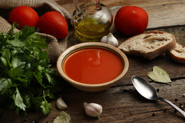 Tomato cream soup with ingredients on wooden background.