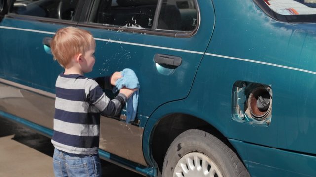 Toddler helping his mother wash car in driveway