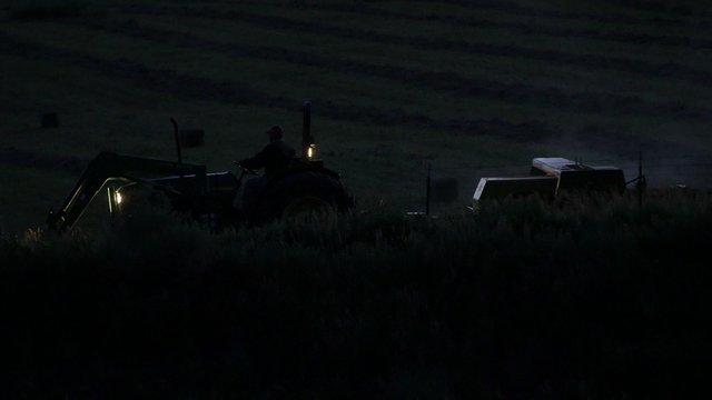 Farmer bailing hay in late evening