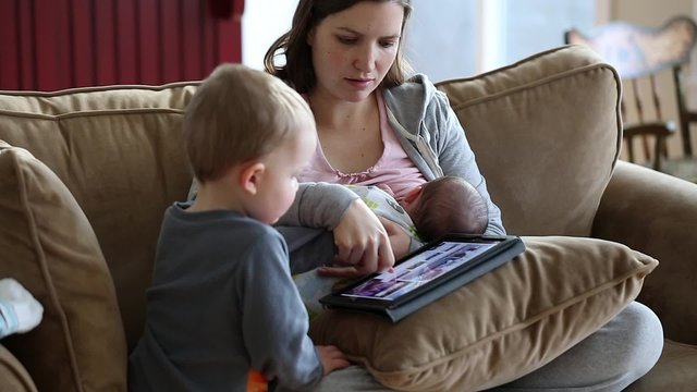mother nursing her boy while toddler plays on ipad