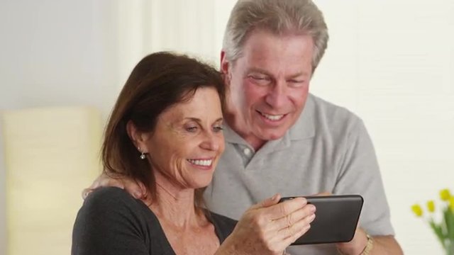 Cute older couple laughing and using new mobile phone