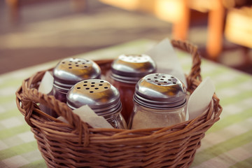 Spices in glass bottles in a wicker basket on the table in cafe.