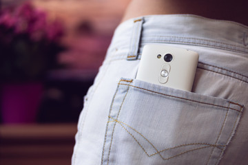 Mobile phone in the back pocket women's jeans on a purple backgr