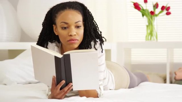 Young black woman reading on bed