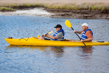 Paddling the Kayak – Two men paddle a yellow kayak in the water.