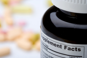 Vitamin Supplement Facts – A bottle of vitamins, with the supplement facts label showing. Vitamins in the background.