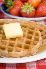 Waffle and Fruit Breakfast – Waffles with butter and syrup. Fresh strawberries in the background.