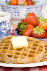 Waffles and Butter – A waffle with butter and syrup. Strawberries in the background.