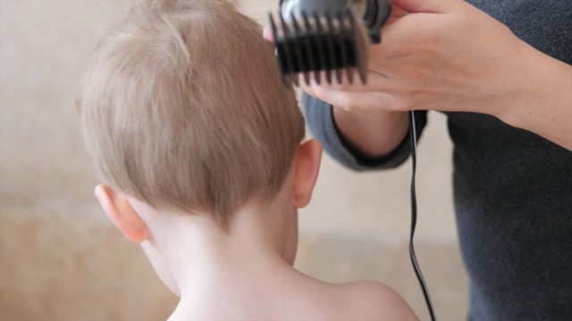 A mother cuts little boys hair