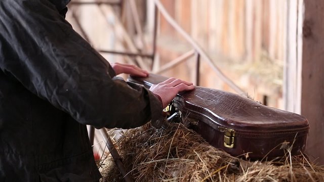 A cowboy opens violin case in an old barn